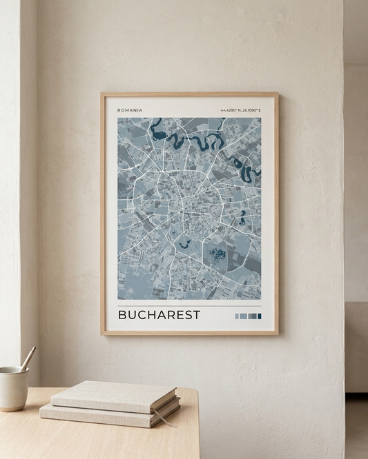 A framed city map poster of Bucharest, Romania, displayed on a textured beige wall above a light wood table with stacked books and a small cup.