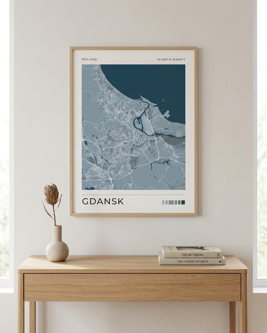 A framed city map print of Gdańsk, Poland, displayed on a light beige wall above a wooden console table with a vase and books.