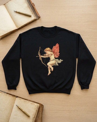 A black crewneck sweatshirt featuring a vintage-style graphic of Cupid with a bow and arrow, laid flat on a light wood background with old books and pens as props.