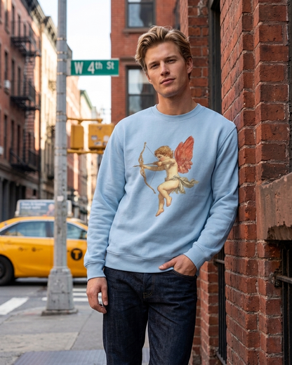 A man wearing a light blue crewneck sweatshirt with a graphic of Cupid on a city street next to a brick wall.