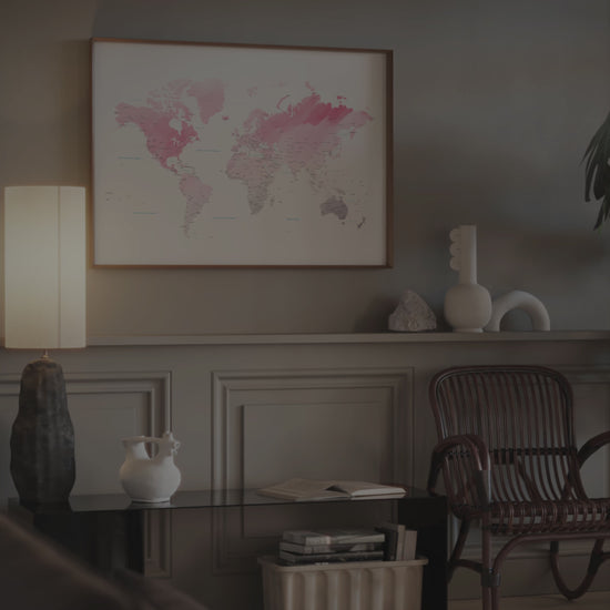 Pink watercolor world map wall art in a dark wood frame.