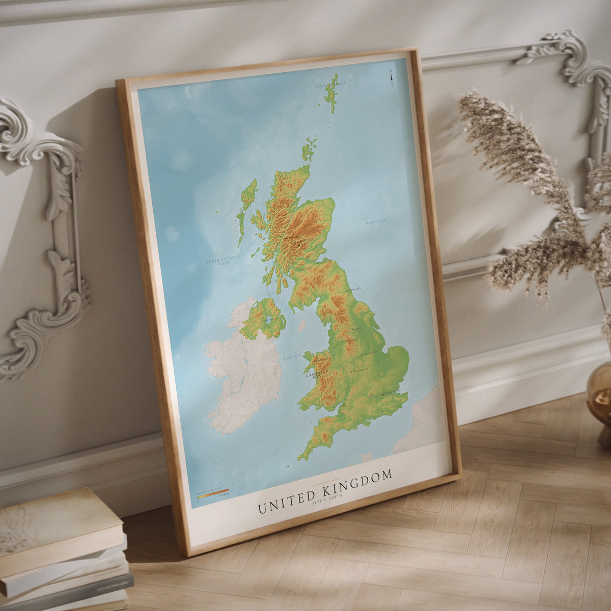 A framed topographical map poster of the United Kingdom hanging on a light-colored wall.