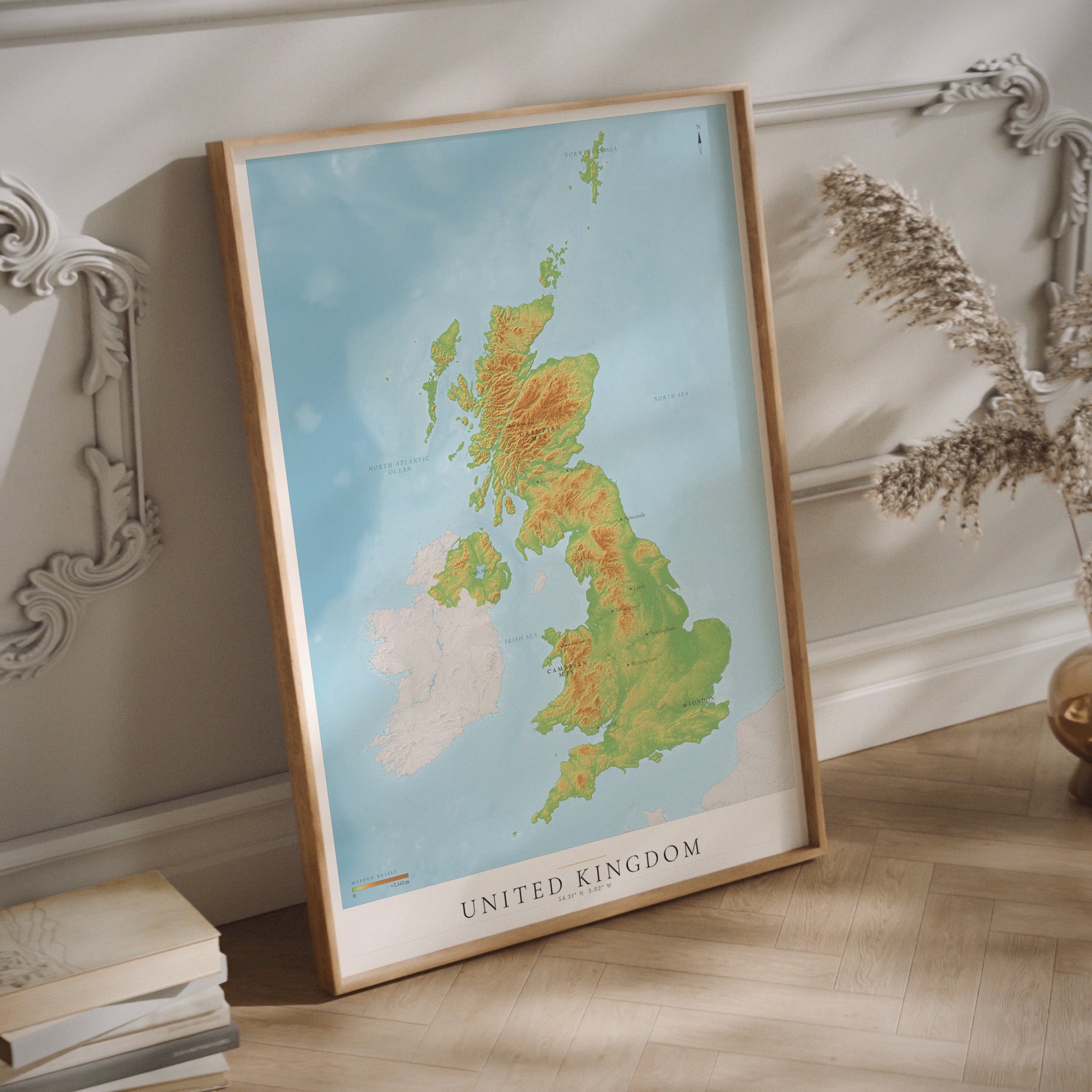 A framed topographical map poster of the United Kingdom hanging on a light-colored wall.