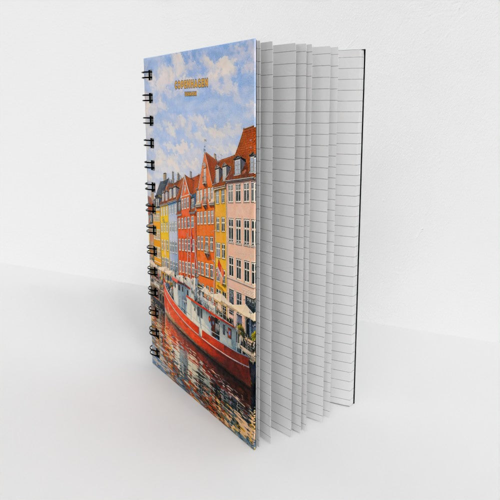 A spiral-bound notebook standing upright on a white surface, showing a colorful city canal scene with buildings and boats on the cover. The notebook has white lined pages visible on the right side.