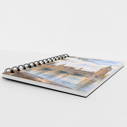 A spiral-bound notebook featuring a scenic print of Big Ben and the London Eye reflected in the water, photographed on a clean white background.