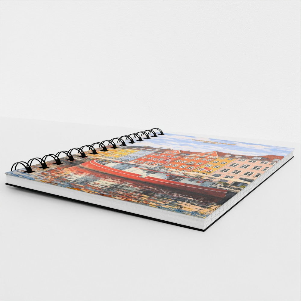 A spiral-bound notebook featuring a colorful cityscape illustration on the cover, photographed at an angle on a clean white background.