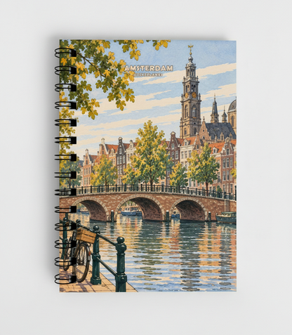A spiral-bound notebook featuring a vintage-style illustration of Amsterdam, with a bridge over water, canal houses, trees, and a bicycle in the foreground, shown on a light gray background.