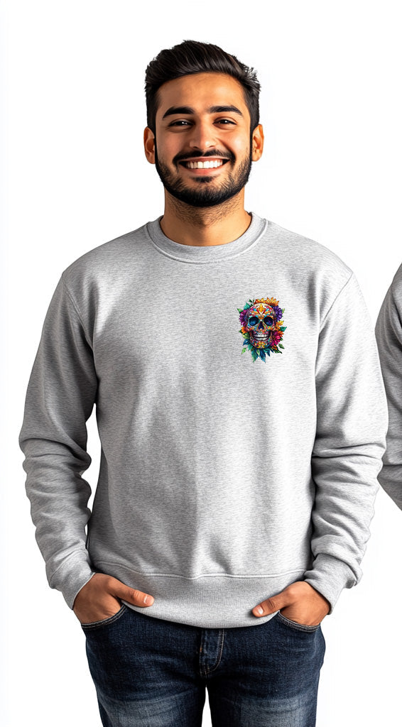 A man modeling a light gray crewneck sweatshirt, showing both front and back views. The front features a small colorful sugar skull graphic on the left chest, while the back features a large, vibrant, multicolored sugar skull graphic with floral details.